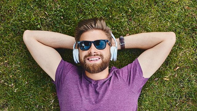 Best summer podcasts man lying on grass wearing headphones